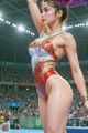 A woman in a red and white leotard standing on a wrestling mat.