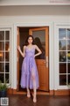 A woman standing in front of a door wearing a purple dress.