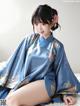 A woman in a blue kimono sitting on a bed.