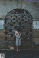 A naked woman standing in front of a stone wall.