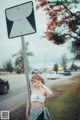 A woman standing next to a road sign on the side of the road.