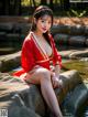 A woman in a red dress sitting on a rock by the water.