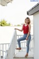 A woman in a red tank top and jeans posing on a porch.