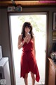 A woman in a red dress standing in front of a window.