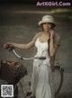 A woman in a white dress and hat standing next to a bike.