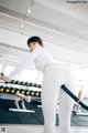 A woman in a white top and white leggings working out in a gym.