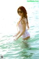 A woman in a white bathing suit and sunglasses standing in the water.