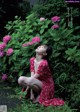 A woman in a red dress sitting in front of pink flowers.