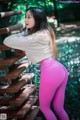 A woman in pink leggings leaning against a wooden fence.