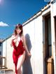 A woman in a red dress leaning against a wall.