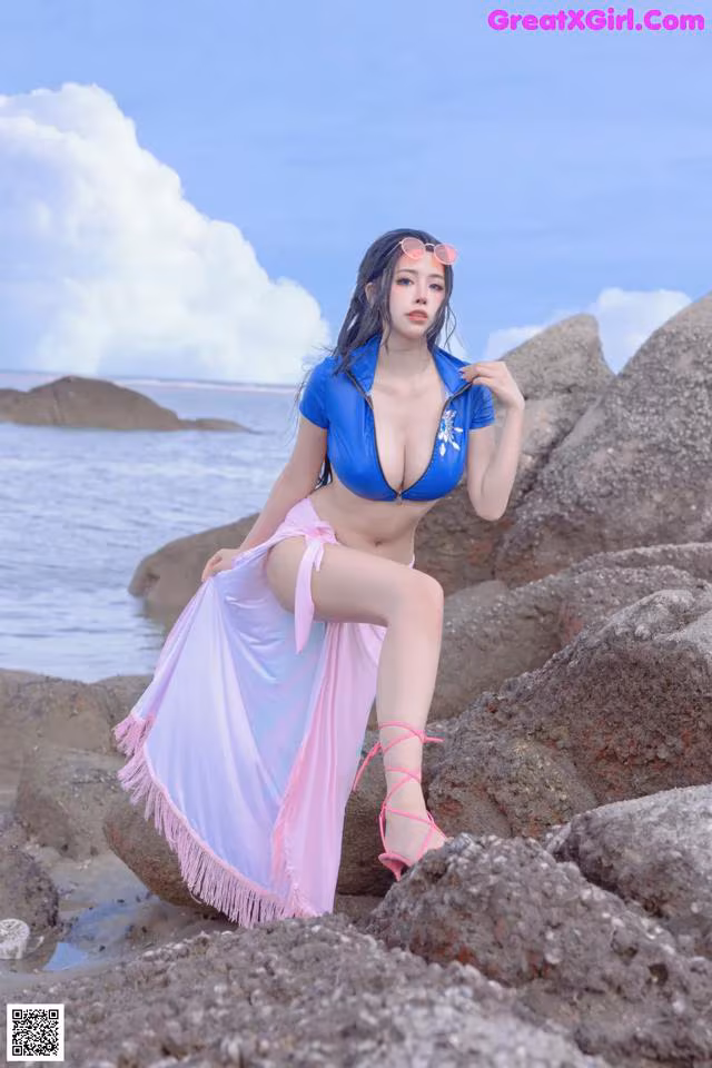 A woman in a blue bikini sitting on a rock by the ocean.