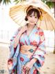 A woman in a blue kimono holding an umbrella on the beach.